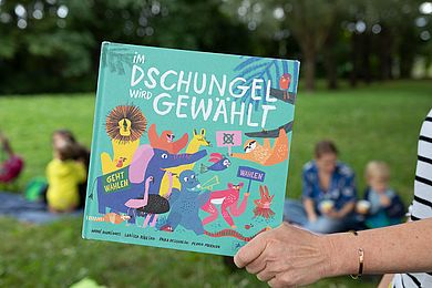 Eine Frau hält ein Buch in der Hand mit der Aufschrift: Im Dschungel wird gewählt.